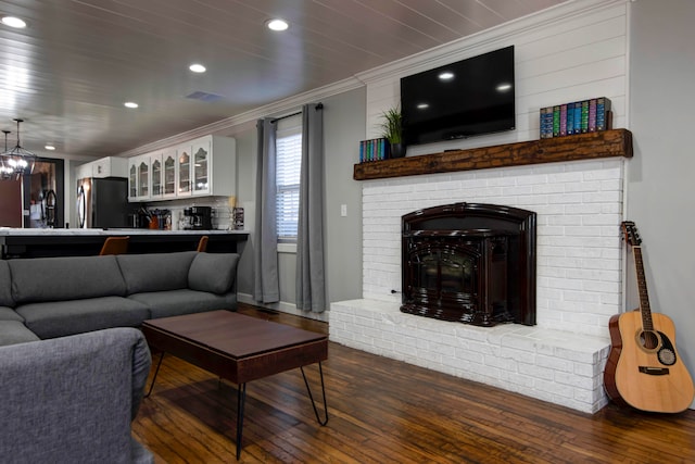 living room with a brick fireplace, ornamental molding, dark wood-type flooring, a chandelier, and bar