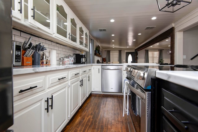 kitchen with backsplash, white cabinets, ornamental molding, dark hardwood / wood-style flooring, and stainless steel appliances