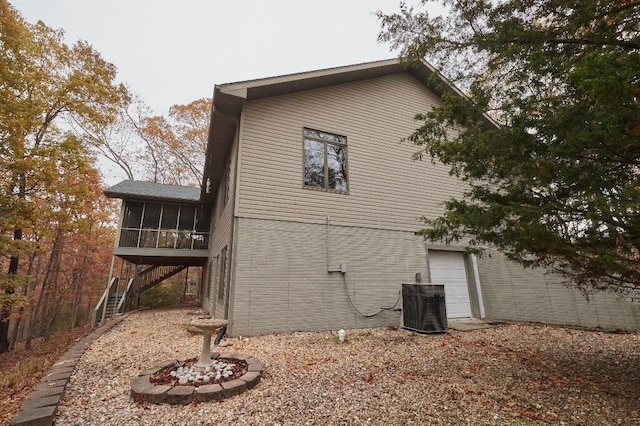 view of property exterior featuring a garage, central AC unit, stairs, and a sunroom