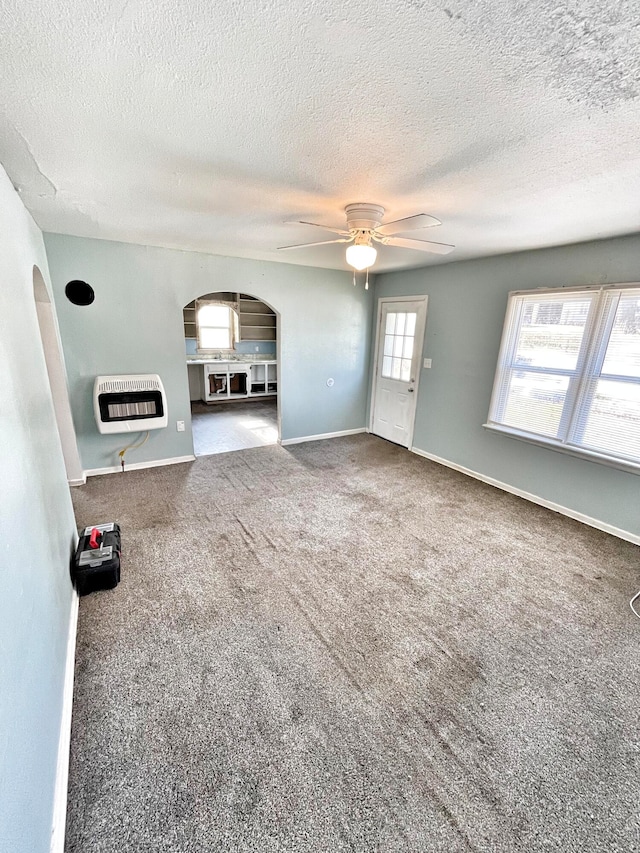 unfurnished living room featuring baseboards, arched walkways, ceiling fan, heating unit, and carpet flooring