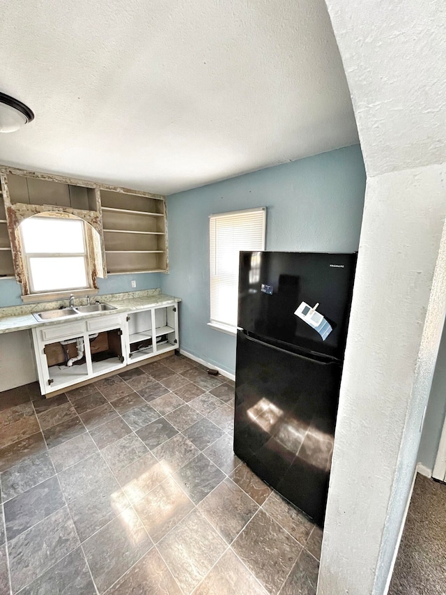 kitchen featuring freestanding refrigerator, stone finish floor, a sink, a textured ceiling, and baseboards