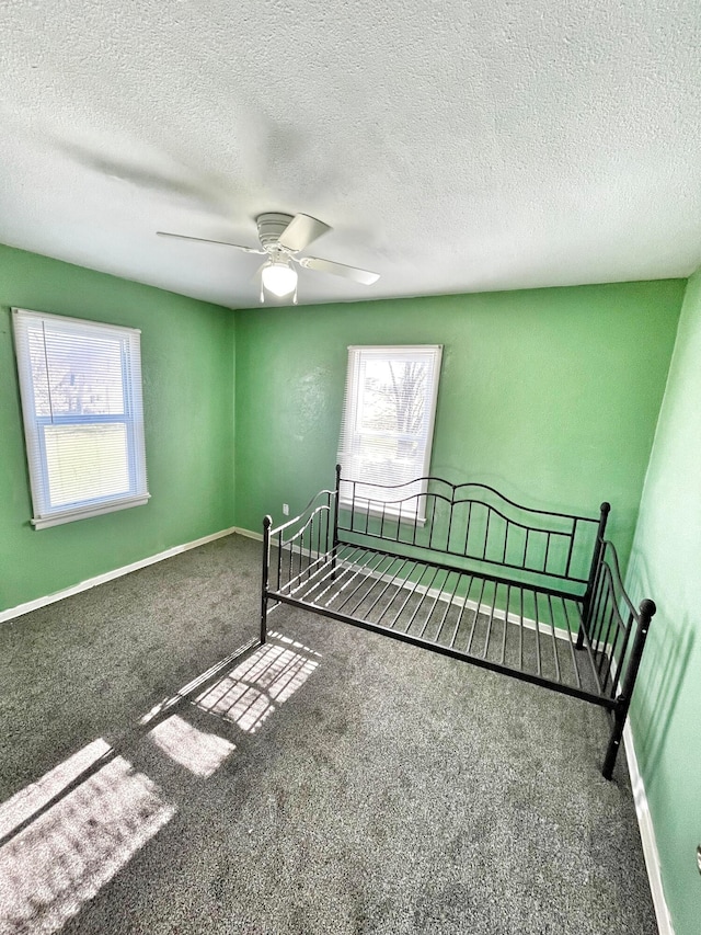 unfurnished bedroom featuring carpet floors, ceiling fan, a textured ceiling, and baseboards