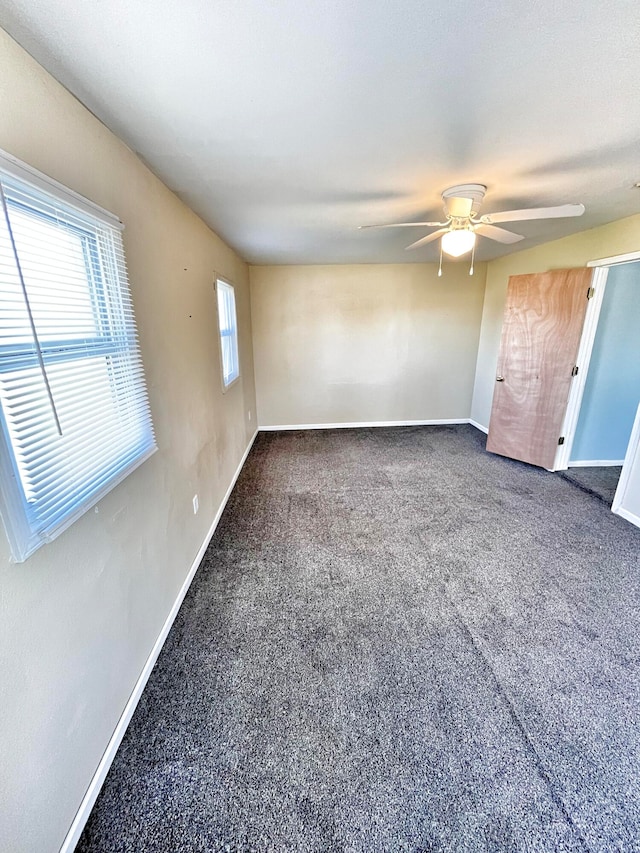 empty room featuring dark colored carpet, a ceiling fan, and baseboards