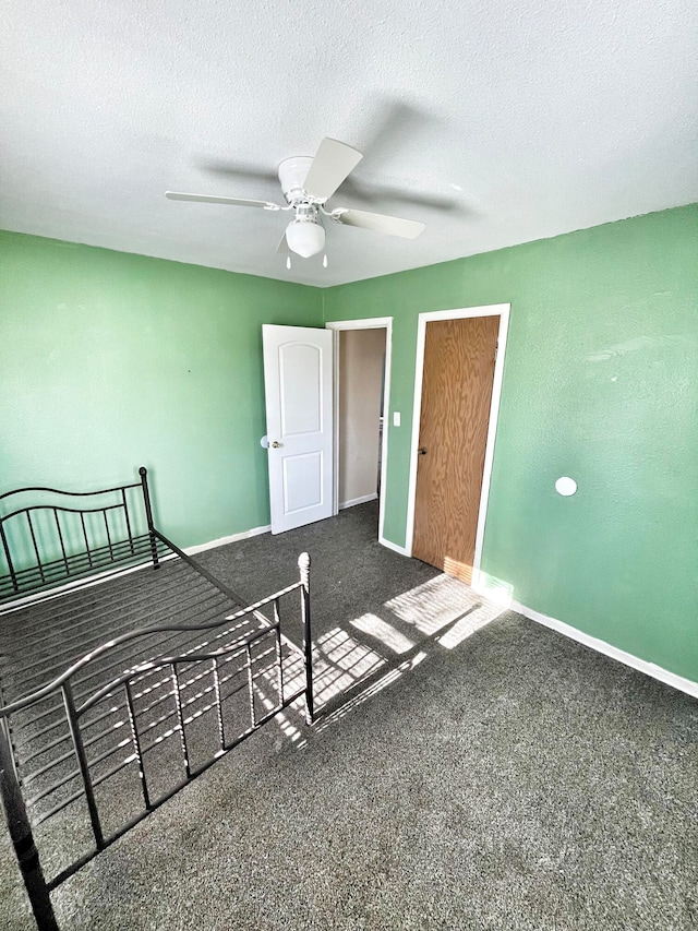 unfurnished bedroom with a textured ceiling, dark colored carpet, ceiling fan, and baseboards