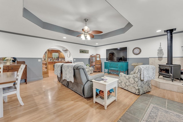 living room with light hardwood / wood-style flooring, a wood stove, ceiling fan, and a tray ceiling