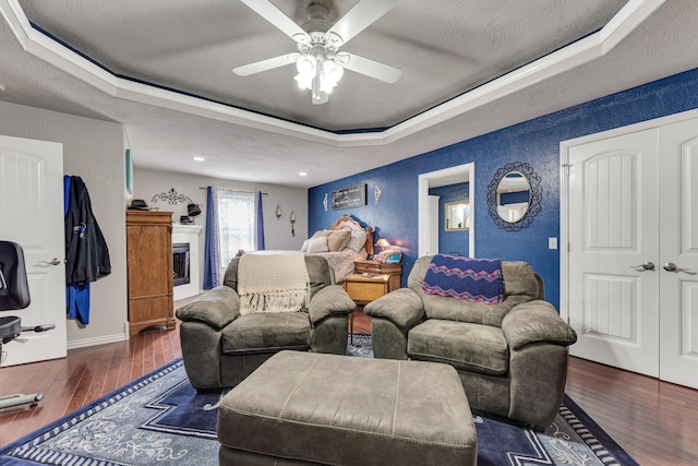 bedroom with a textured ceiling, ceiling fan, dark wood-type flooring, and a tray ceiling