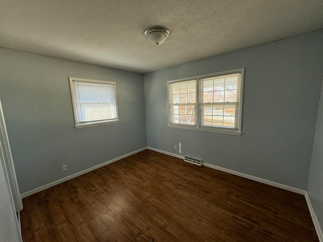 empty room with a textured ceiling and dark hardwood / wood-style floors