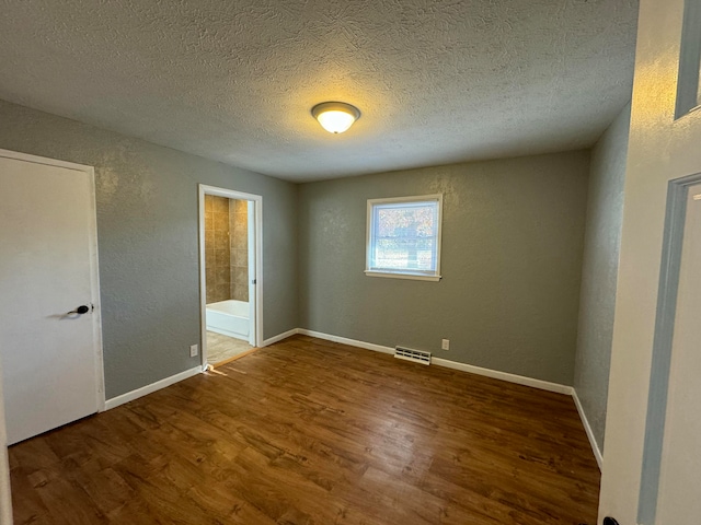 unfurnished bedroom with a textured ceiling, ensuite bathroom, and dark hardwood / wood-style floors