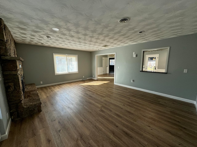 unfurnished living room featuring a stone fireplace, dark hardwood / wood-style flooring, and a textured ceiling