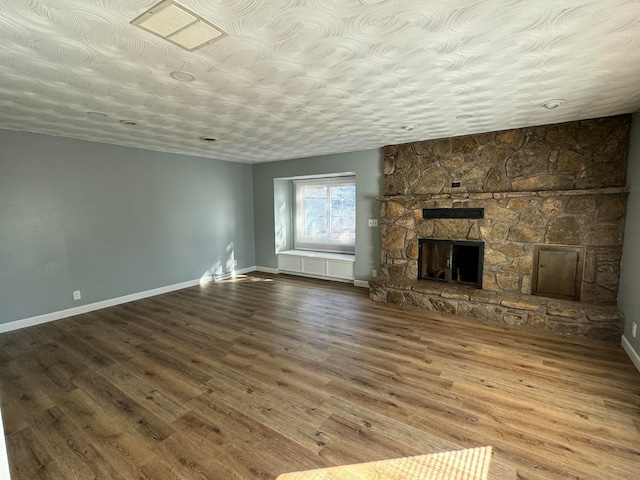 unfurnished living room featuring a stone fireplace, wood-type flooring, and a textured ceiling