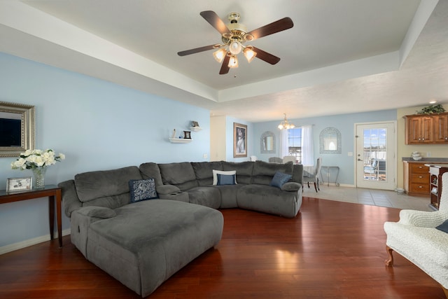 living room with a tray ceiling, ceiling fan with notable chandelier, and dark hardwood / wood-style floors