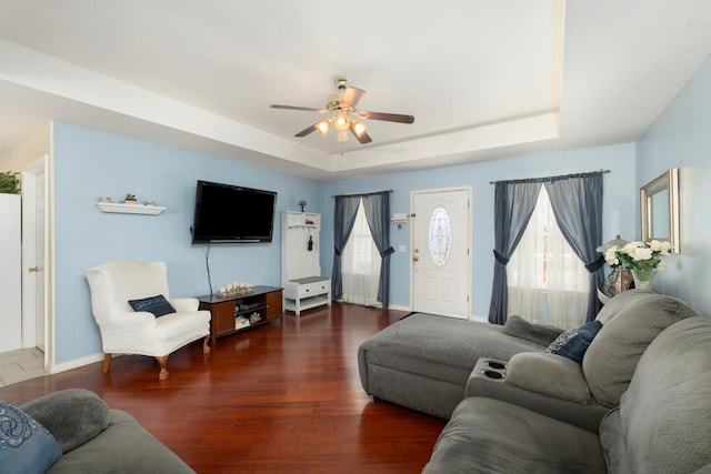 living room with ceiling fan, a raised ceiling, and dark wood-type flooring