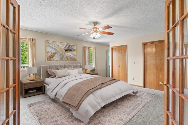 carpeted bedroom with ceiling fan, a textured ceiling, and two closets