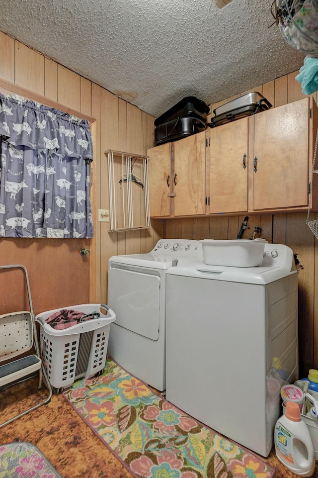 laundry area with cabinets, a textured ceiling, separate washer and dryer, and wooden walls