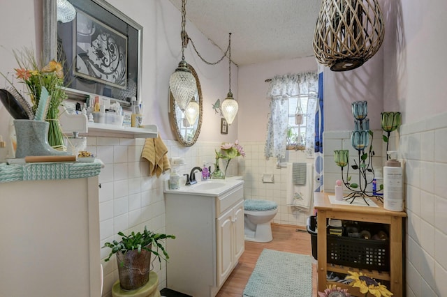 bathroom with vanity, a textured ceiling, hardwood / wood-style flooring, tile walls, and toilet