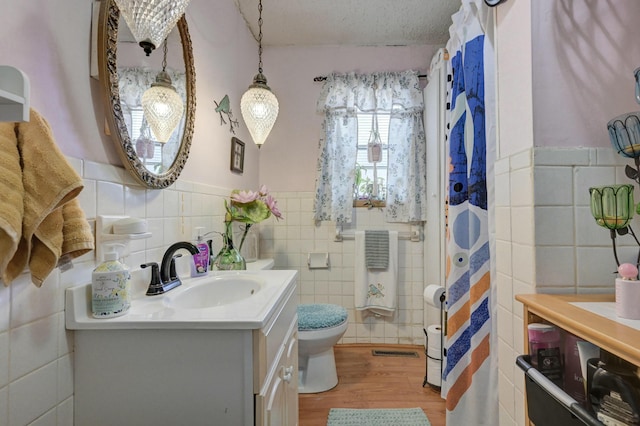 bathroom with vanity, a textured ceiling, hardwood / wood-style flooring, tile walls, and toilet