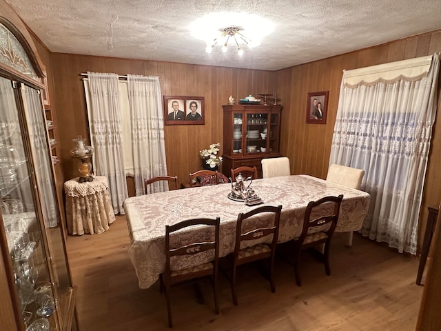 dining room featuring wooden walls, hardwood / wood-style floors, and a textured ceiling