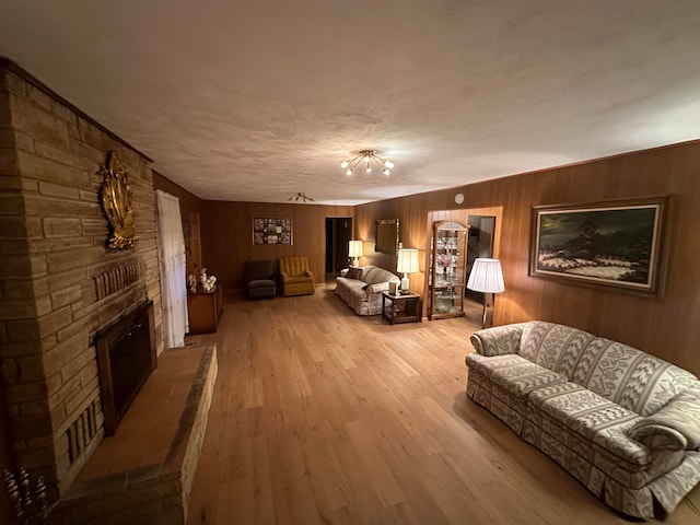 living room featuring wood walls, a stone fireplace, a textured ceiling, and light hardwood / wood-style flooring