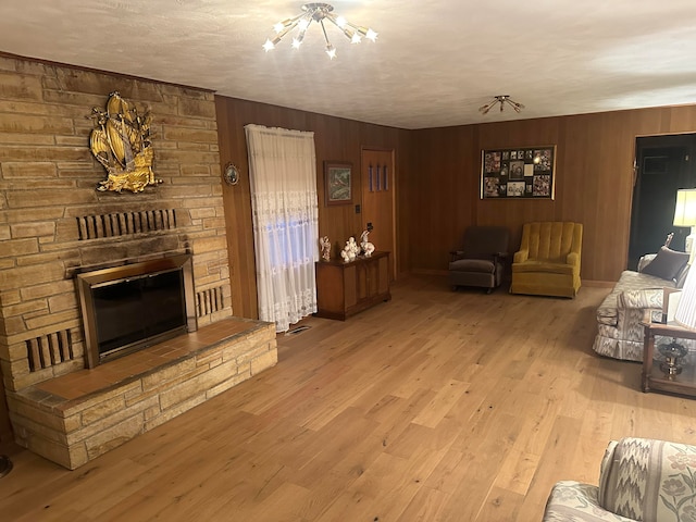 living room featuring wooden walls, a fireplace, an inviting chandelier, and light hardwood / wood-style flooring