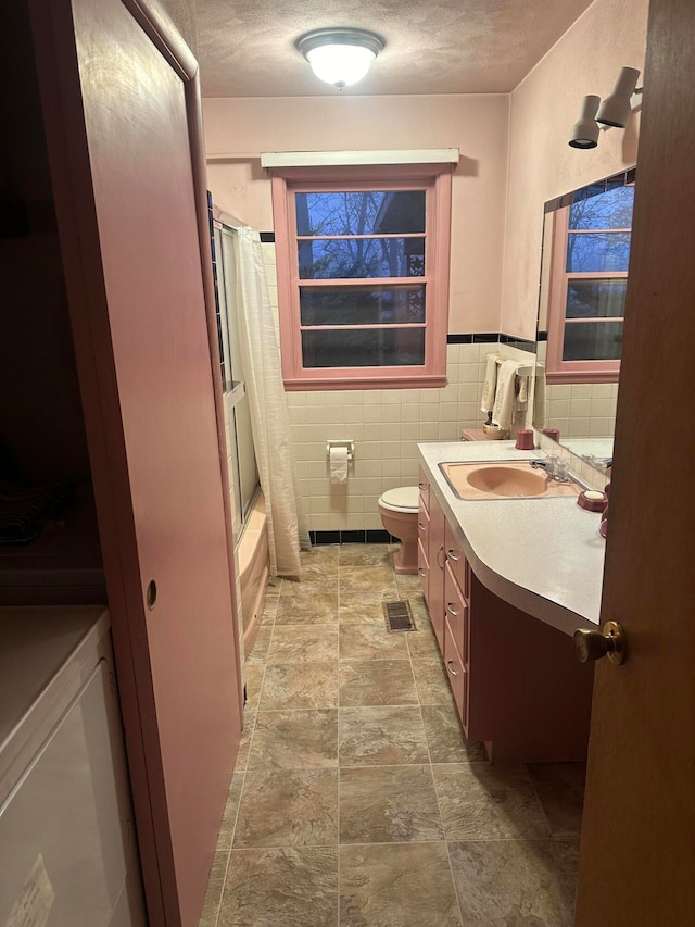 full bathroom with vanity, toilet, a textured ceiling, tile walls, and shower / tub combo with curtain