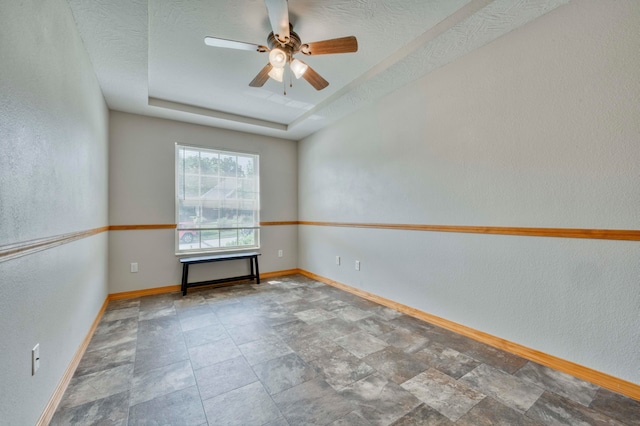 empty room with a tray ceiling, ceiling fan, and a textured ceiling