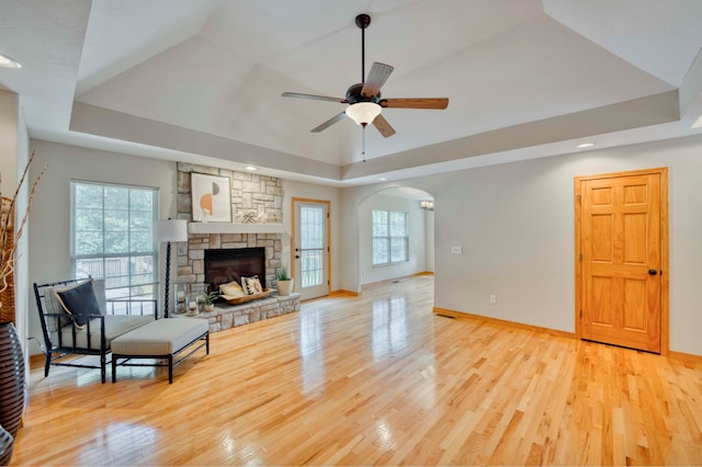 living room featuring a raised ceiling, a fireplace, ceiling fan, and light hardwood / wood-style flooring