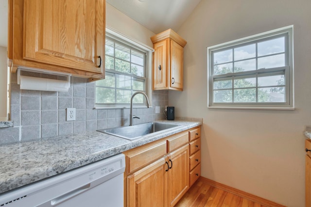 kitchen with dishwasher, sink, backsplash, vaulted ceiling, and light wood-type flooring