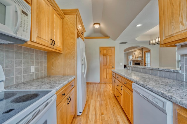 kitchen with a stone fireplace, light hardwood / wood-style flooring, vaulted ceiling, white appliances, and decorative backsplash