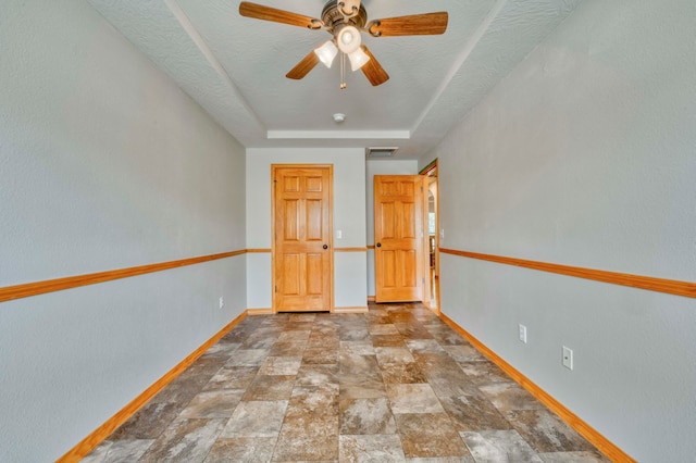 unfurnished bedroom featuring ceiling fan, a textured ceiling, and a tray ceiling