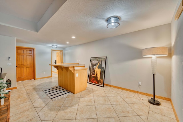 kitchen with tile counters, kitchen peninsula, a textured ceiling, a kitchen bar, and light tile patterned floors