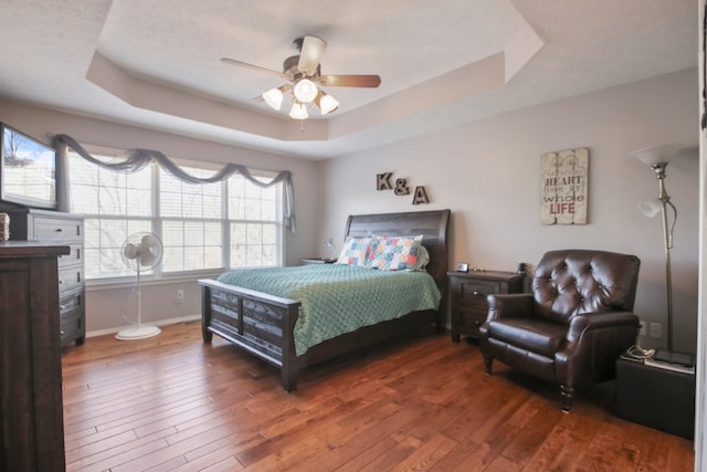 bedroom with hardwood / wood-style flooring, ceiling fan, and a tray ceiling