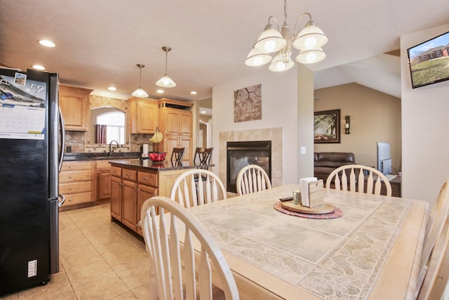 dining area with lofted ceiling, sink, light tile patterned floors, a notable chandelier, and a tiled fireplace