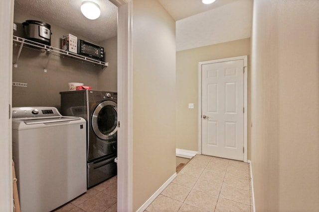 clothes washing area featuring light tile patterned flooring, washing machine and clothes dryer, and a textured ceiling