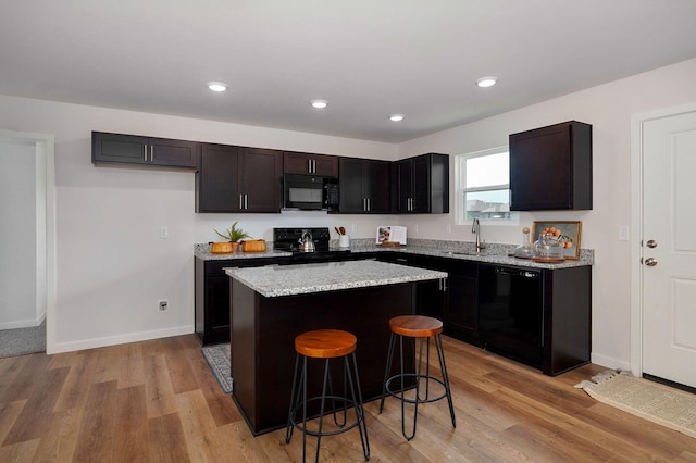 kitchen with black appliances, sink, light hardwood / wood-style floors, a kitchen island, and a kitchen bar