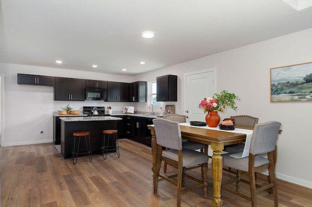 kitchen with light stone countertops, a breakfast bar area, a kitchen island, black appliances, and light wood-type flooring