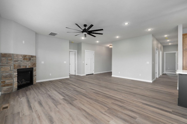 unfurnished living room featuring hardwood / wood-style flooring, ceiling fan, and a stone fireplace