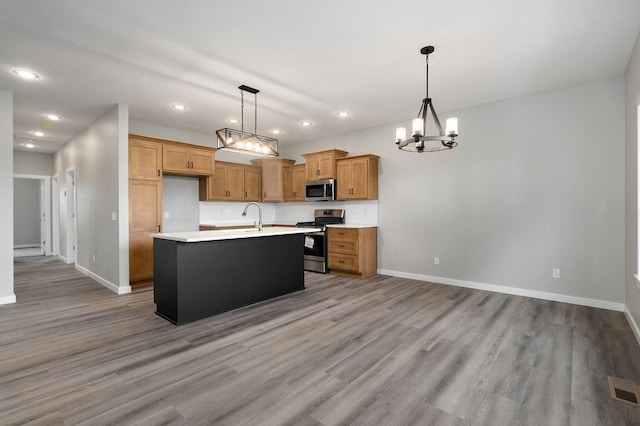 kitchen featuring appliances with stainless steel finishes, pendant lighting, a chandelier, light hardwood / wood-style floors, and an island with sink