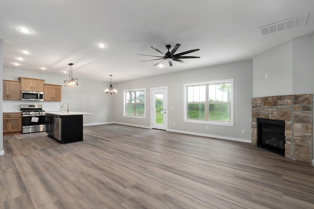 kitchen with hanging light fixtures, stainless steel appliances, dark wood-type flooring, a fireplace, and a center island with sink