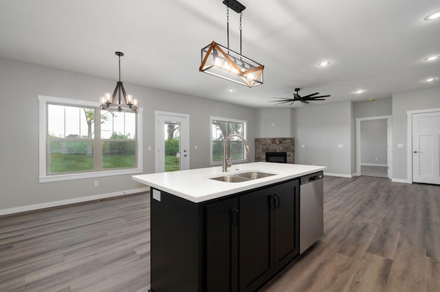 kitchen with stainless steel dishwasher, ceiling fan with notable chandelier, sink, pendant lighting, and an island with sink