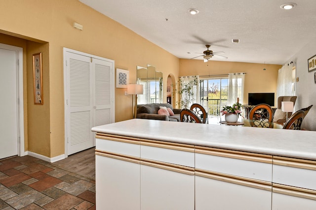 kitchen featuring a textured ceiling, white cabinetry, ceiling fan, and lofted ceiling