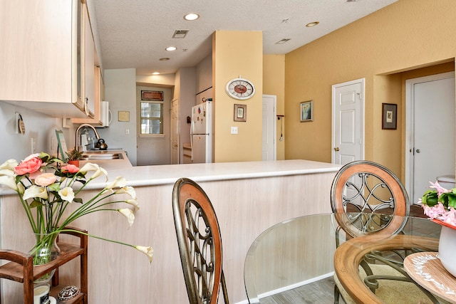 kitchen featuring kitchen peninsula, a textured ceiling, white appliances, sink, and hardwood / wood-style floors