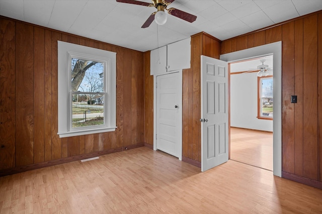 unfurnished bedroom with a closet, light hardwood / wood-style flooring, ceiling fan, and wood walls