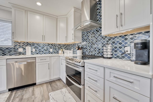 kitchen featuring wall chimney exhaust hood, white cabinetry, light hardwood / wood-style flooring, appliances with stainless steel finishes, and backsplash