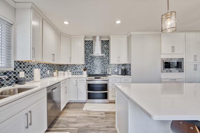 kitchen featuring appliances with stainless steel finishes, pendant lighting, white cabinets, backsplash, and wall chimney exhaust hood