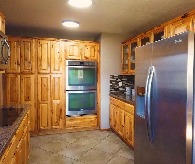 kitchen with appliances with stainless steel finishes, tasteful backsplash, light tile patterned floors, and dark stone countertops