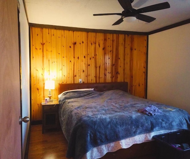 bedroom with ceiling fan, ornamental molding, dark wood-type flooring, and wooden walls