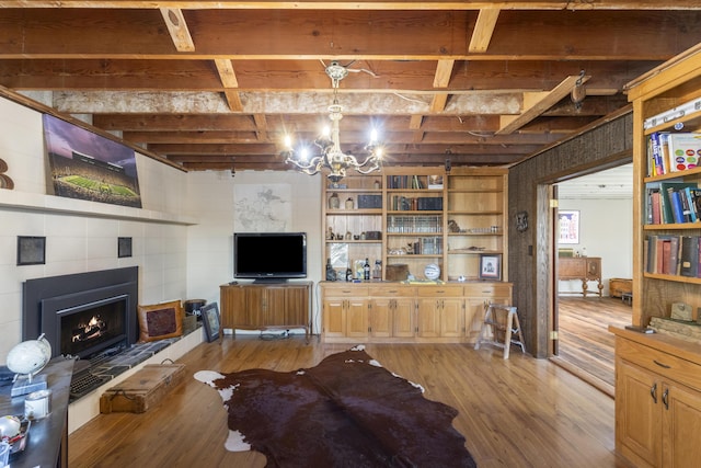 living room with a tiled fireplace, beamed ceiling, light hardwood / wood-style floors, and an inviting chandelier