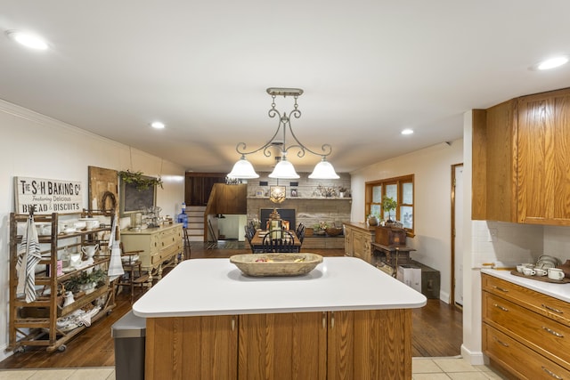 kitchen with a center island, hanging light fixtures, light wood-type flooring, ornamental molding, and tasteful backsplash