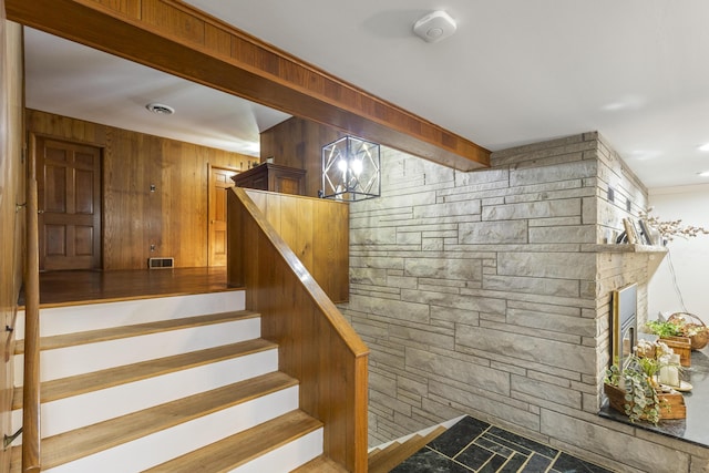 stairway with a chandelier, a fireplace, and wood walls