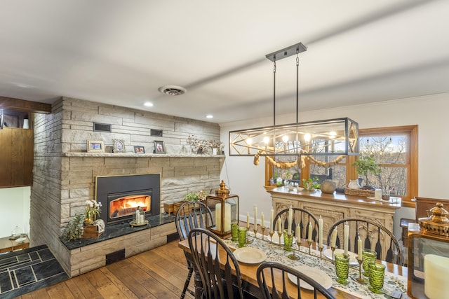 dining space with hardwood / wood-style floors, a stone fireplace, and a chandelier